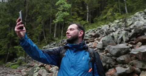 A man stands in the forest on large stones and takes out a smartphone Video stock 243604443