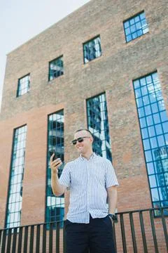 Man stands in front of a brick building while looking at his smartphone in .. Stock Photos