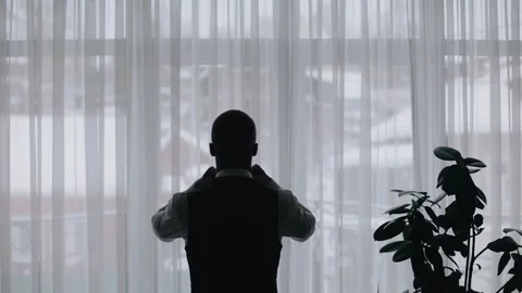 A man stands in front of a bright window and gets dressed Stock Footage 277632541