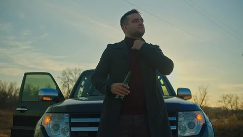 A man stands in front of the car, he stands with a bottle of beer, looks left an Stock Footage 121625707