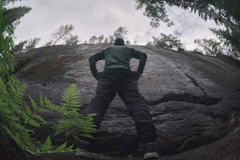 A man stands in front of an insurmountable vertical granite wall. low angle Foto stock