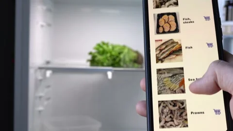 A man stands in front of an open empty refrigerator and scrolls through an as Stock Footage 196709774