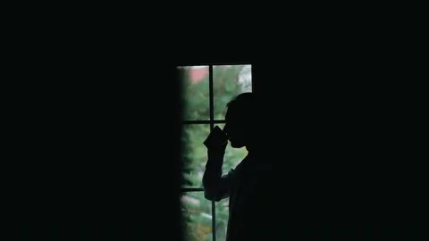 A man stands in front of the window and drinks from a mug Stock Footage 196721335