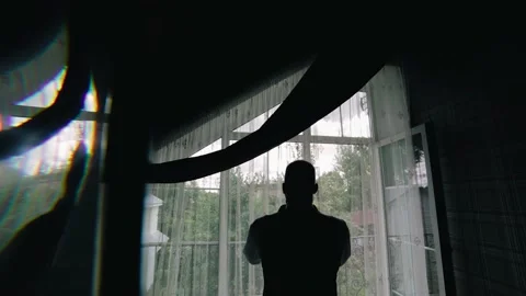 A man stands in front of the window and adjusts the collar of his shirt Stock Footage 229726551