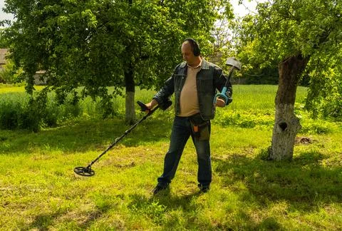 A man stands in a green field using a metal detector. He searches carefully.. Stock Photos