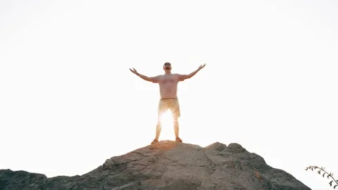 A man stands on a high mountain facing the sun and victoriously opens his hands Stock Footage 160758482
