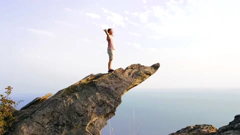 Man stands on a high steep cliff with his hands open and enjoys the scenery Stock Footage 160758485