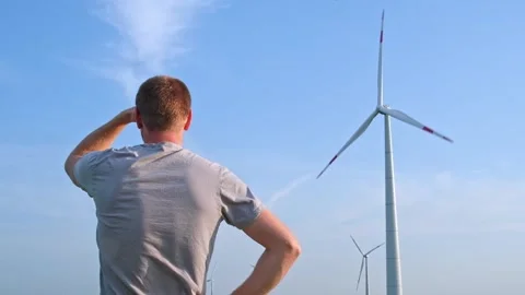 Man stands with his back and looks at the wind turbine. Wind Energy Park. Stock Footage 242443466