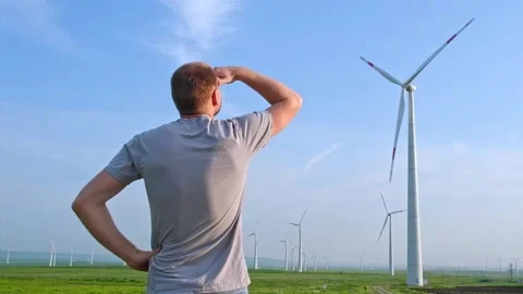 Man stands with his back and looks at the wind turbine. Wind Energy Park. Stock Footage 242443504