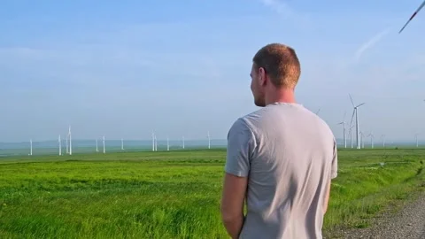 Man stands with his back and looks at the wind turbine. Wind Energy Park. Stock Footage 242443516
