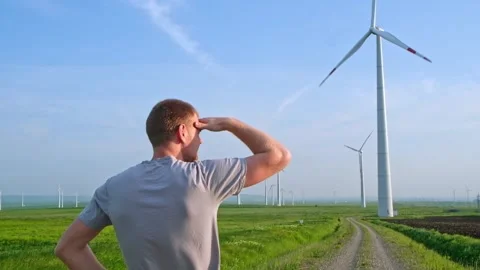 Man stands with his back and looks at the wind turbine. Wind Energy Park. Stock Footage 242443545