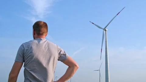 Man stands with his back and looks at the wind turbine. Wind Energy Park. Stock Footage 243288957