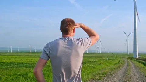 Man stands with his back and looks at the wind turbine. Wind Energy Park. Stock Footage 243792408