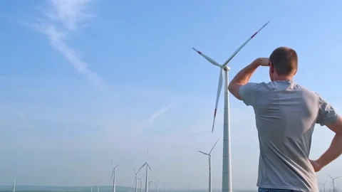 Man stands with his back and looks at the wind turbine. Wind Energy Park. Stock Footage 244803855