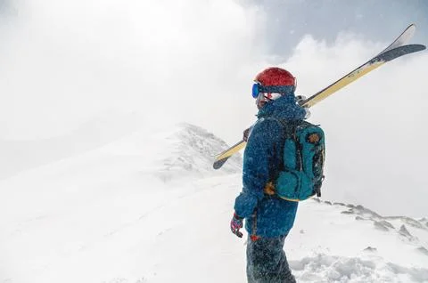 Man stands with his back to the camera with alpine skis on his shoulder against Stock Photos