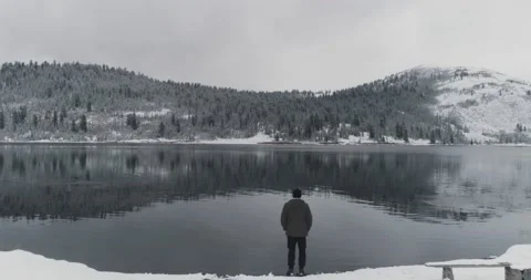 Man stands with his back on shore of lake in mountains in winter Stock Footage 163520451