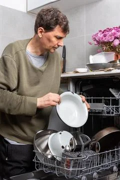 A man stands in his kitchen taking clean dishes out of the dishwasher. He foc Stockfoto's