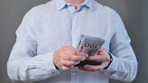 A man stands indoors and counts money taken from his wallet. He appears to be in Stockbeeldmateriaal 338300098