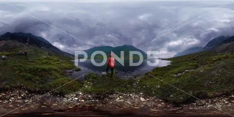Man stands by lake in red jacket in cloudy weather. Spherical panorama 360vr Stock Photos