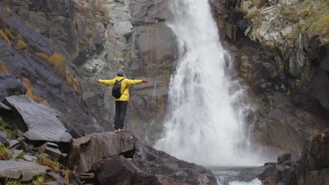 Man stands on large stone, looking at waterfall Video stock 227023088