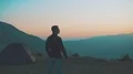The man stands near the camping tent on the mountain on a sunset background 4k or 4k+ Resolution