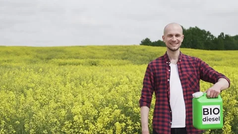 Man stands next to a blooming rapeseed field and holds jerrycan witch biodiesel Stock Footage 134476173