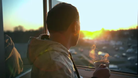 A man stands by an open window with a mug of hot drink during sunset Stock Footage 130814926