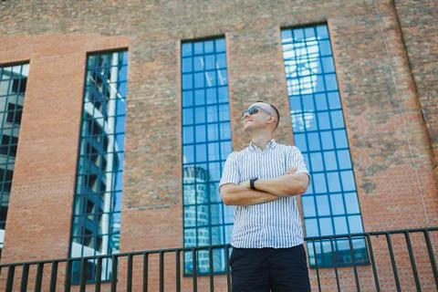 Man stands outside a building with large windows and red brick walls while .. Stock Photos