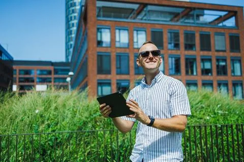 Man stands outside with a tablet in a modern urban area under a clear blue sk Stock Photos