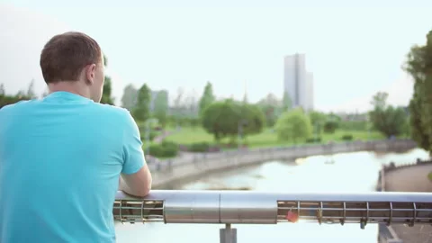 Man stands in a park on a bridge and looks at the river, camera movement, copy Stock Footage 135305220