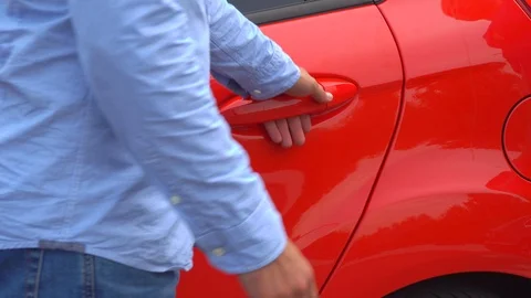 Man stands at red car and openes back door for young woman. She comes to it and Stock Footage 99778749