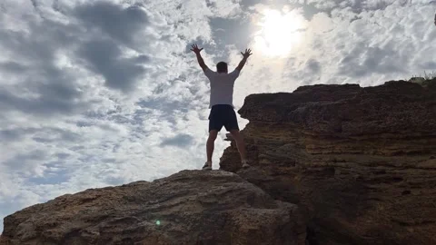 Man stands on rock peak overlooking vast landscape. Victory and freedom concept Stock-Footage 337219996