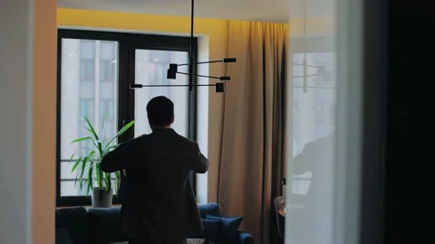 A man stands in a room in front of a window and gets dressed Stock Footage 223477329
