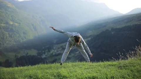 Man stands rotating hands cross touching toes warming up outdoors in mountains Stock Footage 79970800