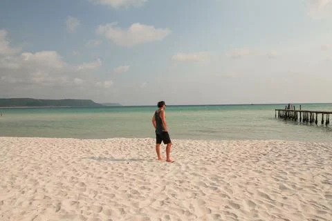 A man stands on a sandy beach looking out at the calm ocean Stock Photos