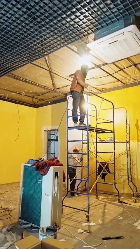 Man stands on the scaffold tower indoors installing light and decor on the Stock Footage 337717372