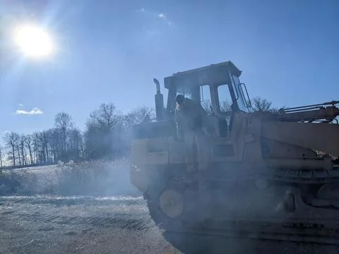 A man stands on the side of a track loader with smoke coming out of the exhaust Stock Photos