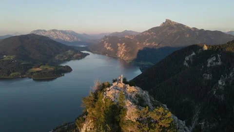 Man stands at a summit cross in summer. Below it is a large mountain lake Stock Footage 165455397