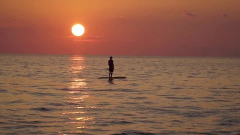 A man stands on a surfboard on a sunset background Stock Footage 119855691