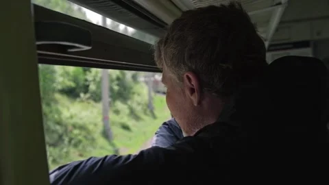 Man stands at train window and looks out window at landscapes and passing trains Stock Footage 234049943