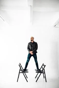 Man stands on two chairs in a studio with white background during daytime Stock Photos