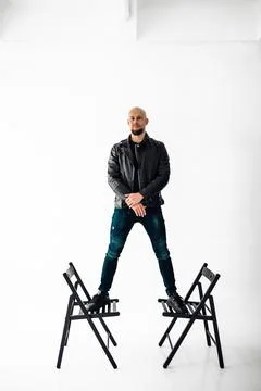Man stands on two chairs in a studio with white background during a creative Stock Photos