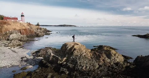 Man Stands Victoriously on a Cliff in Maine next to Lighthouse Stock Footage