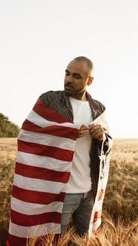 Man stands in wheat field while holding American flag during sunset Stock Photos