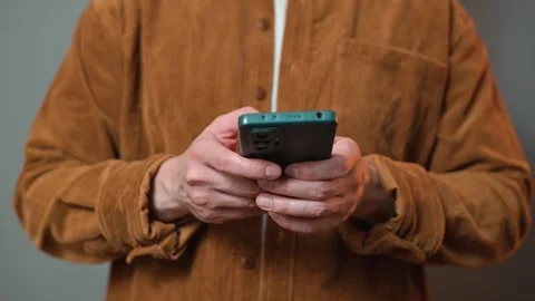 A man stands while holding a smartphone in both hands. He appears focused on the 스톡 동영상 337643213