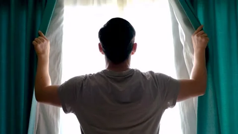 Man stands at window and opens turquoise curtains rear view. Stock Footage 231961098
