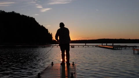 A man stands on a wooden dock at sunset in the evening fishing Video stock 278144792