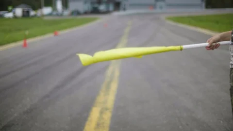 Man stands with a yellow flag at the start-finish line. Flag waving in the wind Stock Footage 129920843