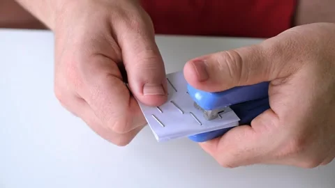 Man stapling sheets of paper with a blue office stapler. Males hands hold a Stock Footage 321862001