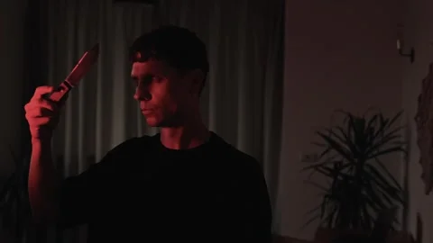 Man staring at his reflection in a knife blade during a moment of moral conflict Vídeos de archivo 347301603